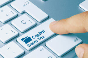 A hand pressing on a keyboard button with the words capital gains tax on a second home
