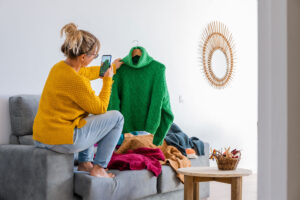 a woman navigating vinted taxes who is on a sofa taking photos of clothing to sell